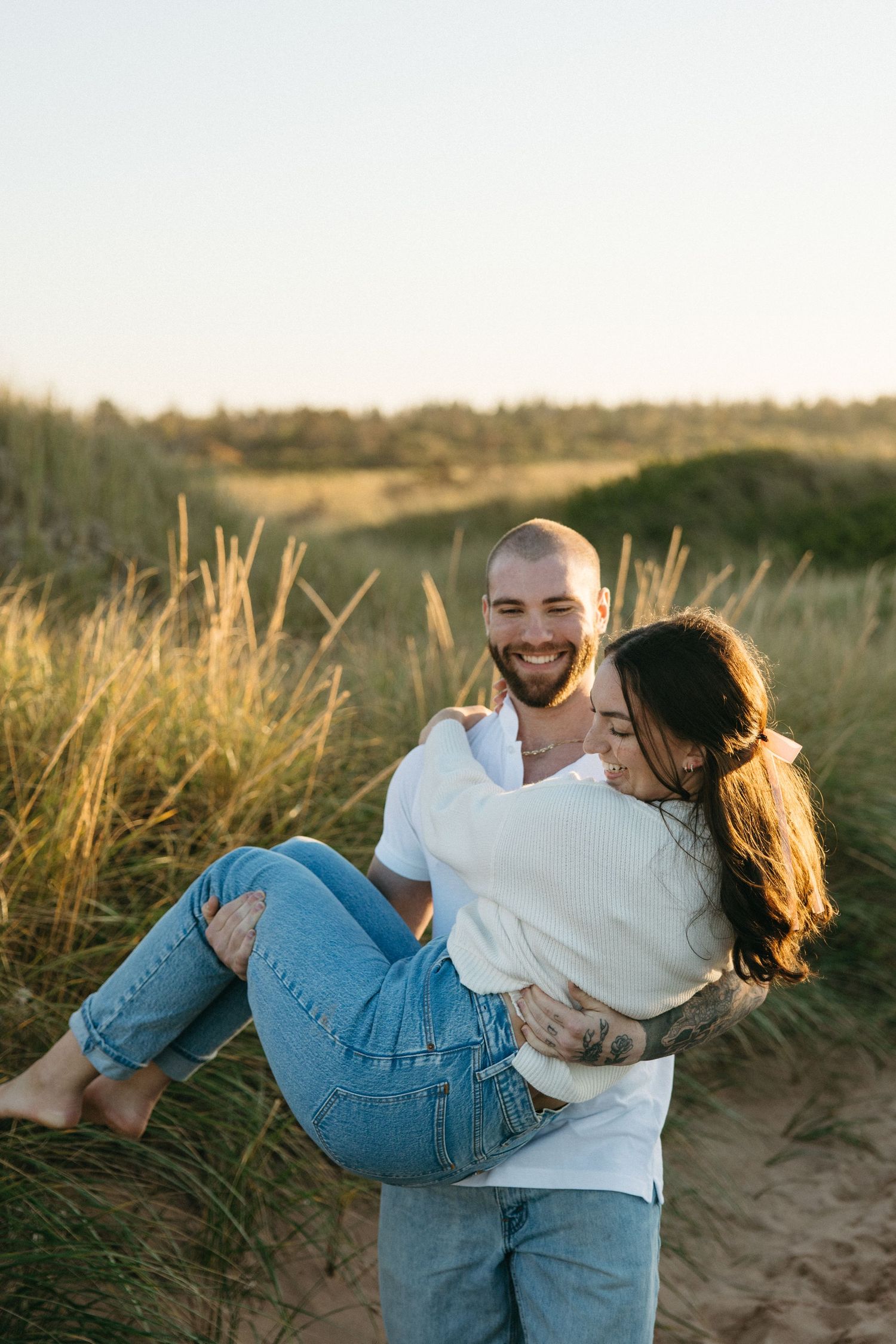A couple laughs while dancing and spinning in a field at golden hour.