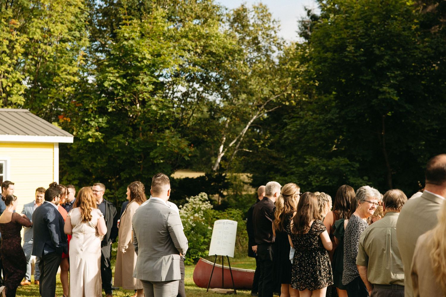 Outdoor wedding ceremony setup with guests standing in rows on a grassy lawn.
