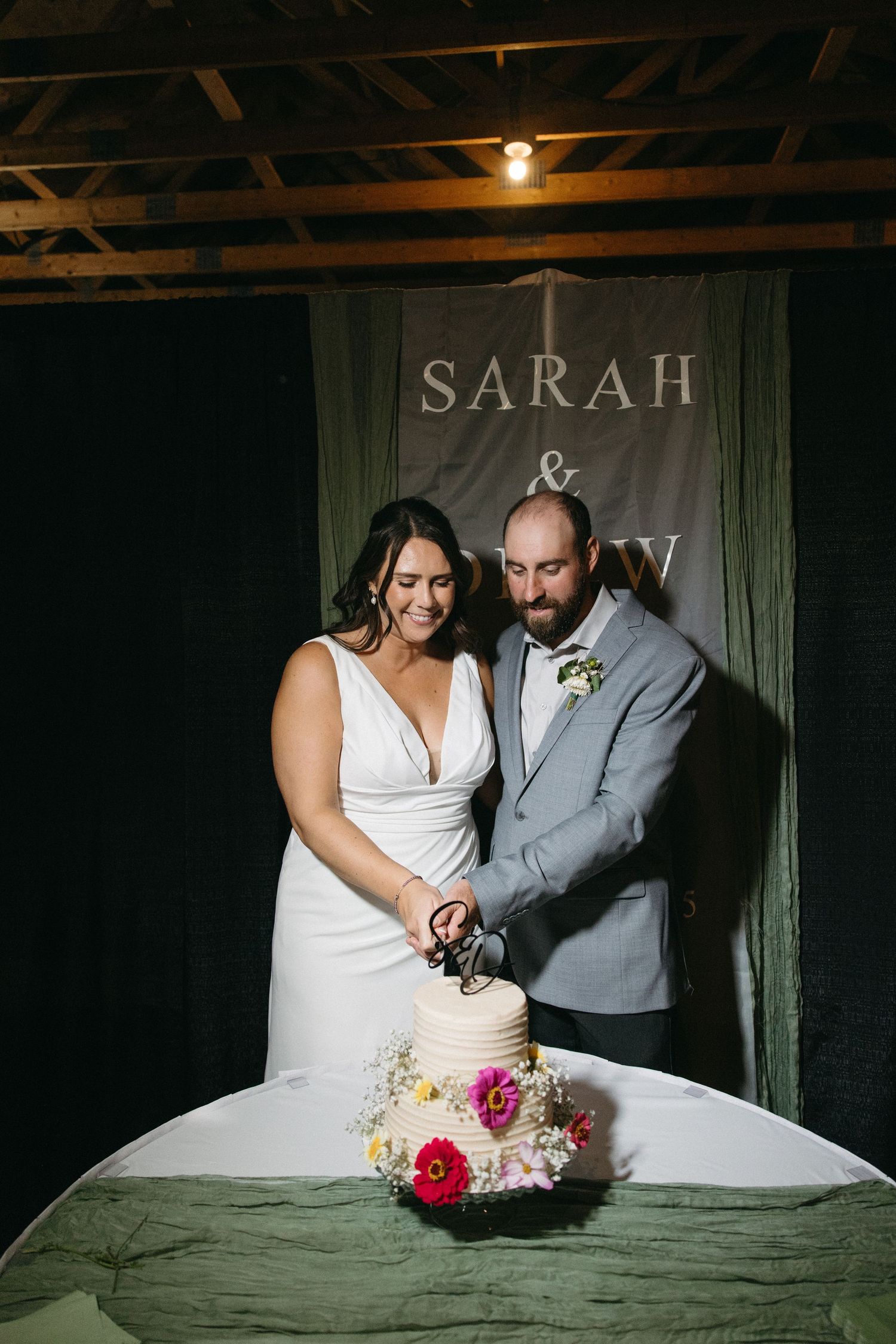 Couple cutting their wedding cake together in a rustic barn setting with decorative text on the wall.