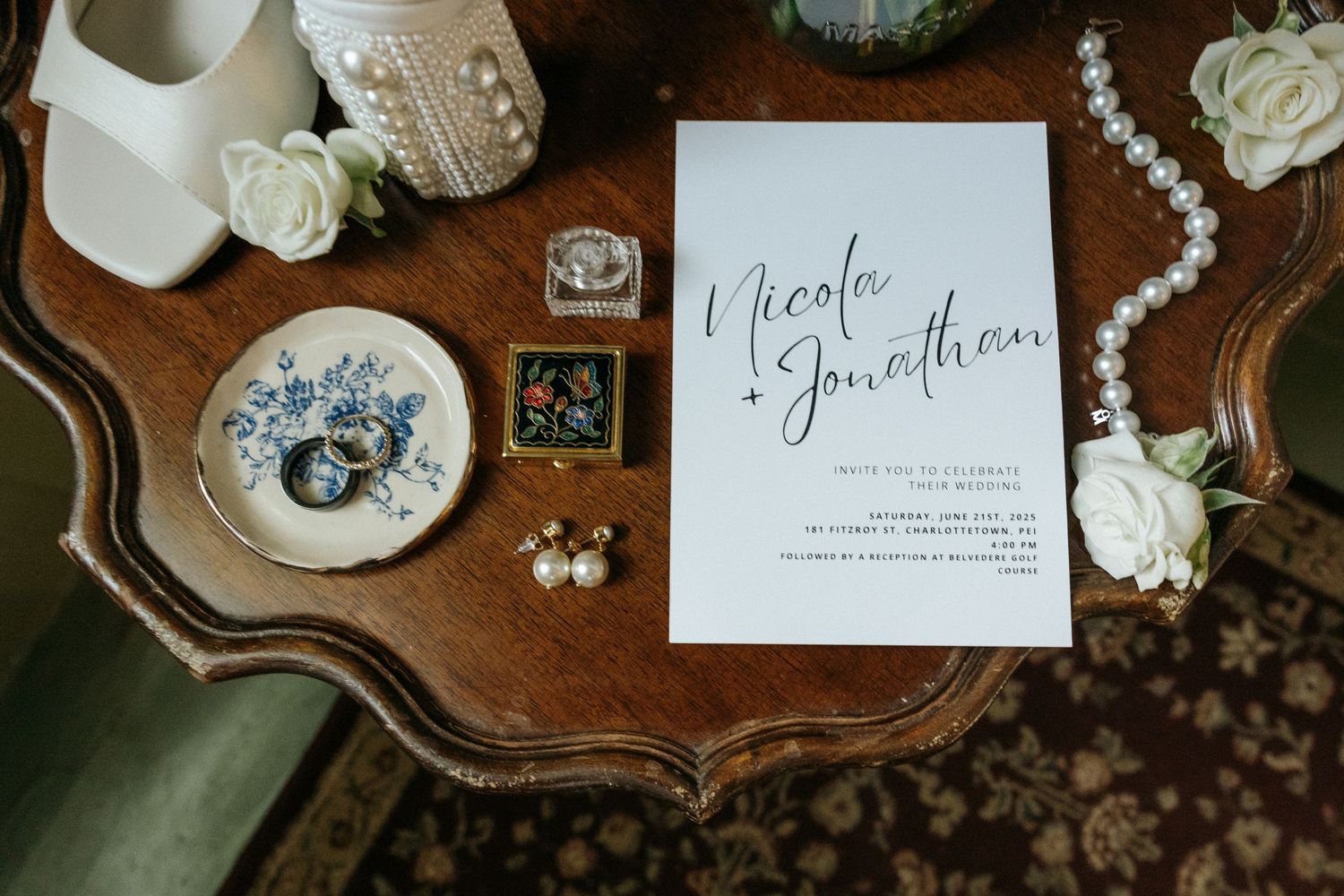 Wedding details including invitation, pearls, and white roses arranged on a vintage wooden surface.