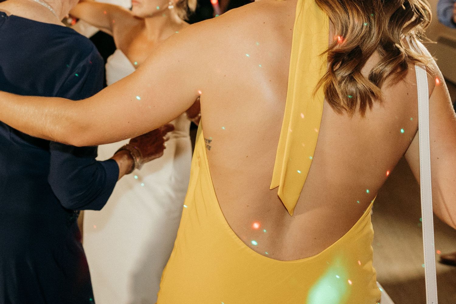 Person in a yellow dress dances at a wedding reception under string lights.