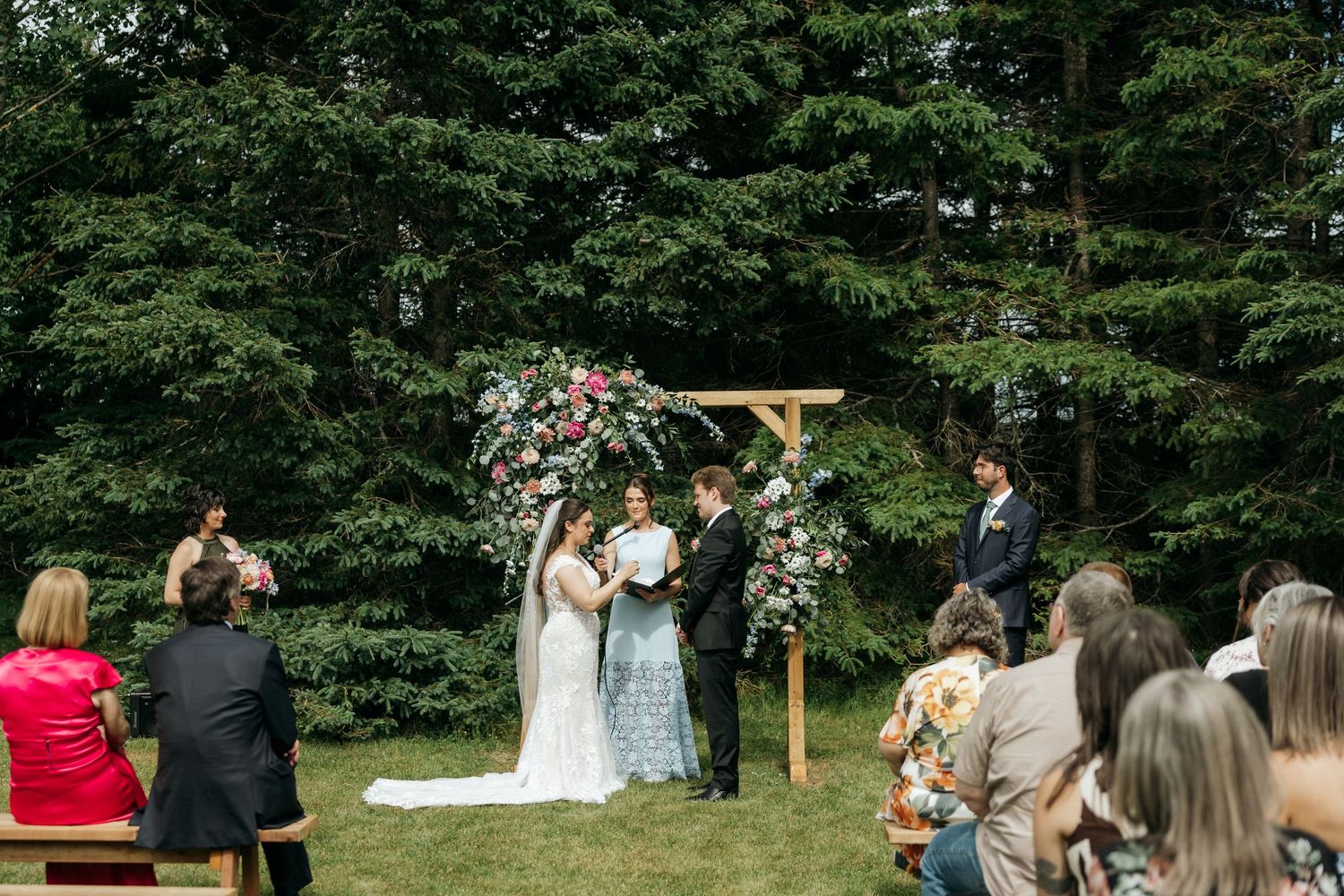 Panoramic view of outdoor wedding ceremony with floral decorated wooden arch.