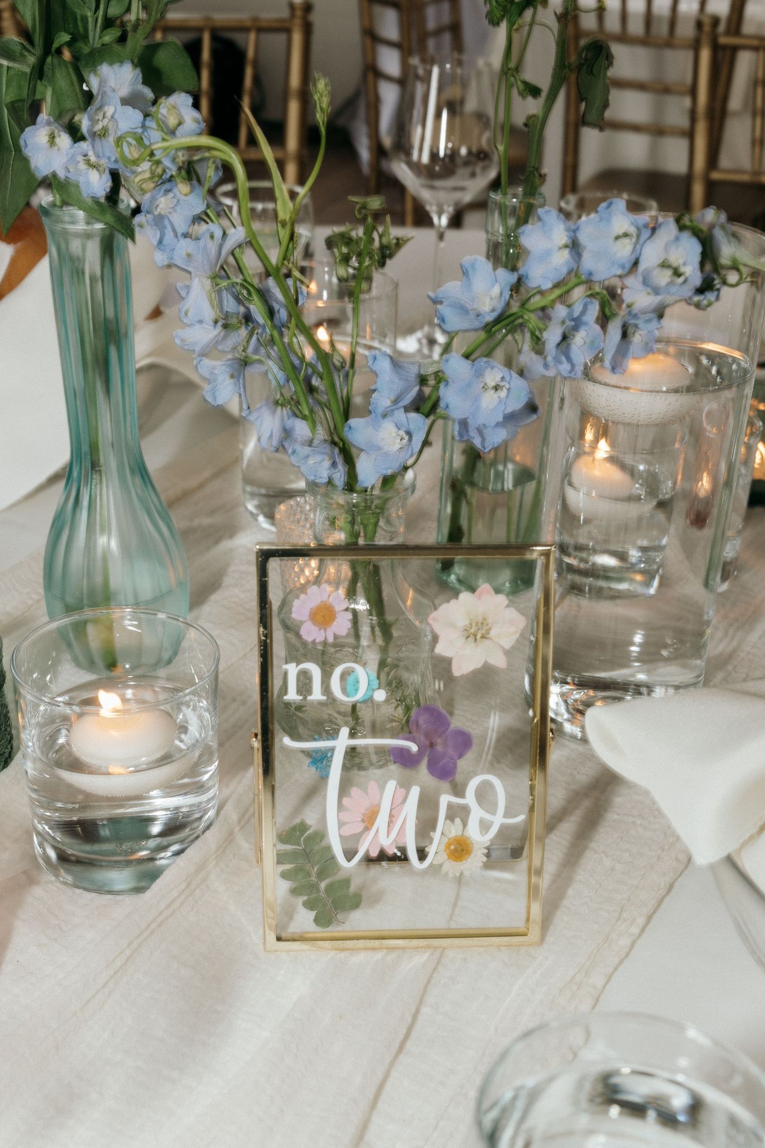 Wedding reception tables decorated with blue glass vases, white flowers, and tea lights creating a romantic atmosphere.