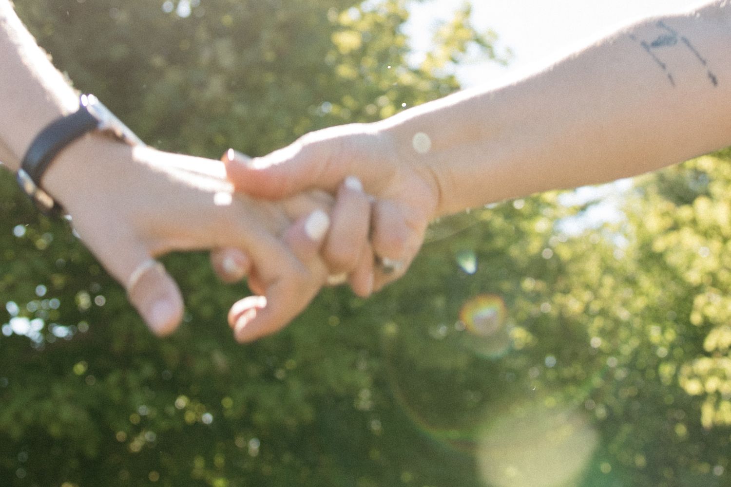 Close-up of two hands holding each other against a sunny outdoor background.