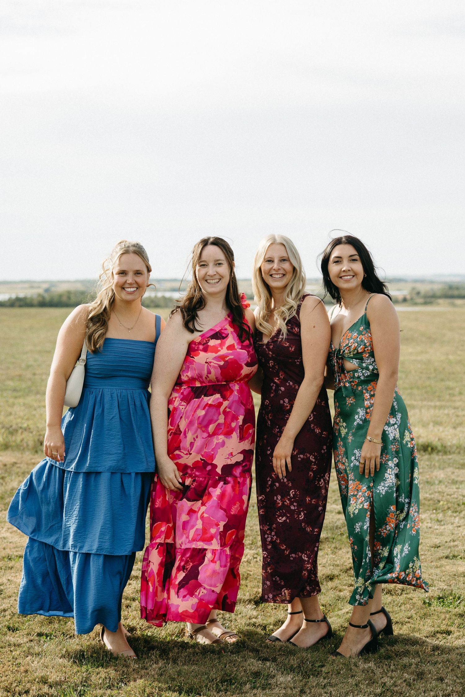 Group wearing colorful summer dresses standing together in a grassy field.