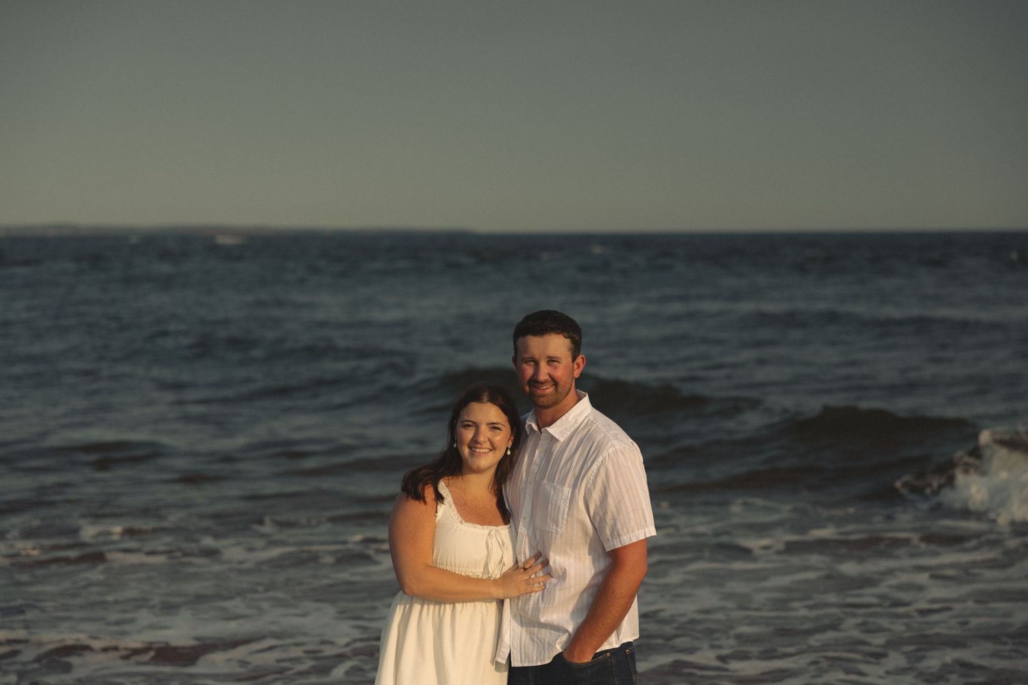 Romantic beach scene with couple embracing near ocean waves.