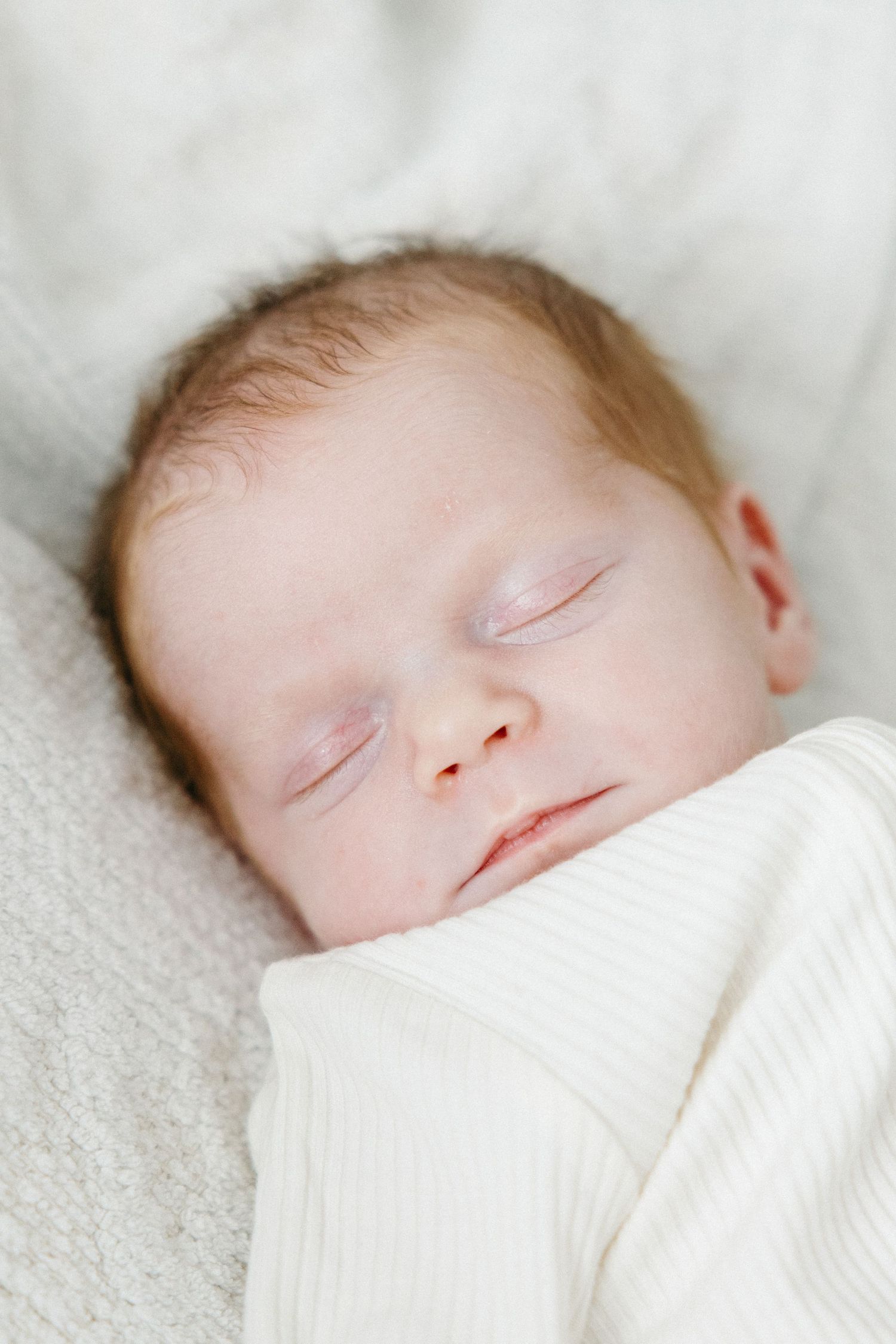 Peaceful sleeping newborn baby wrapped in white blanket against soft white background.