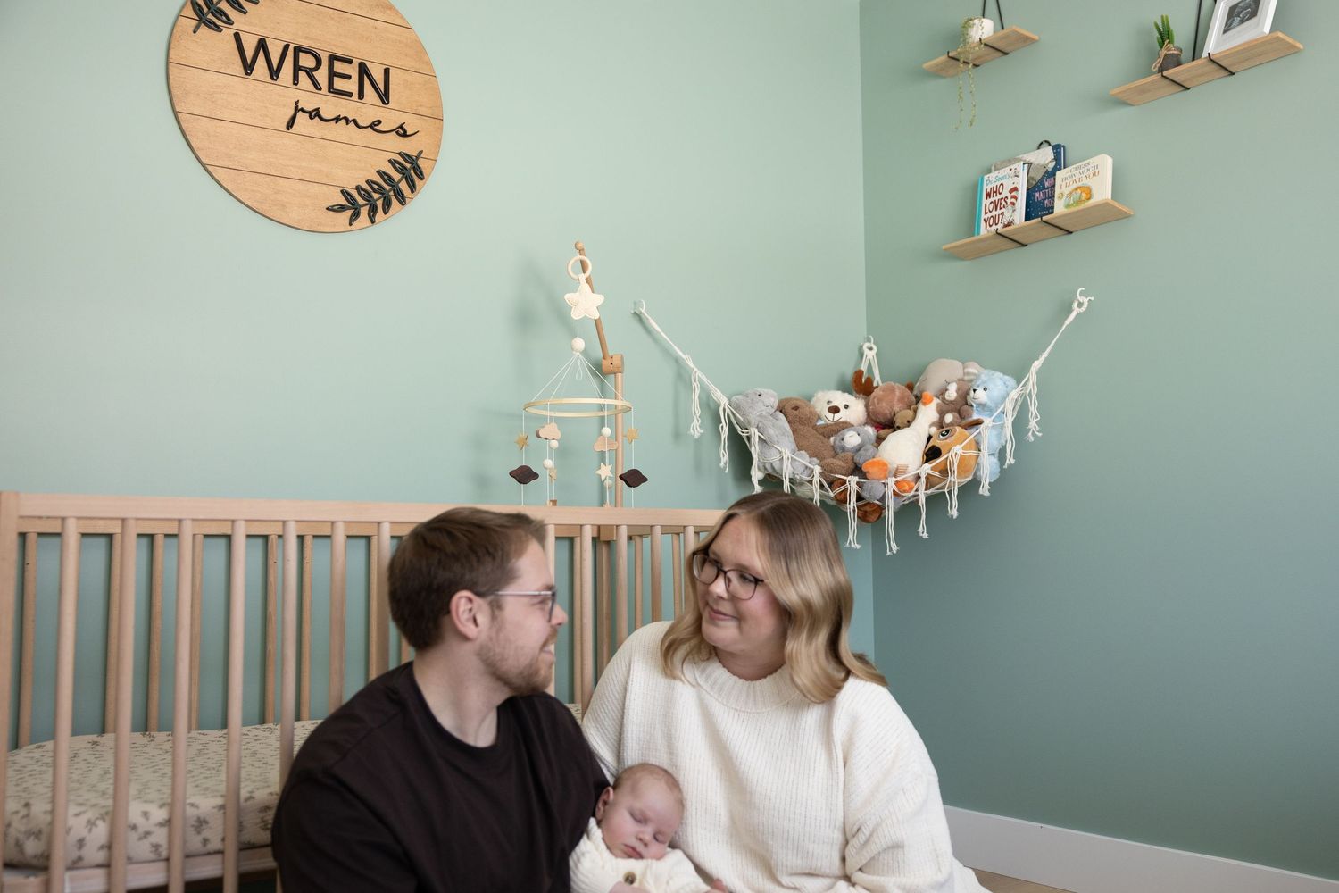 A nursery room with mint green walls features a wooden Wren sign and decorative floating shelves above a crib.