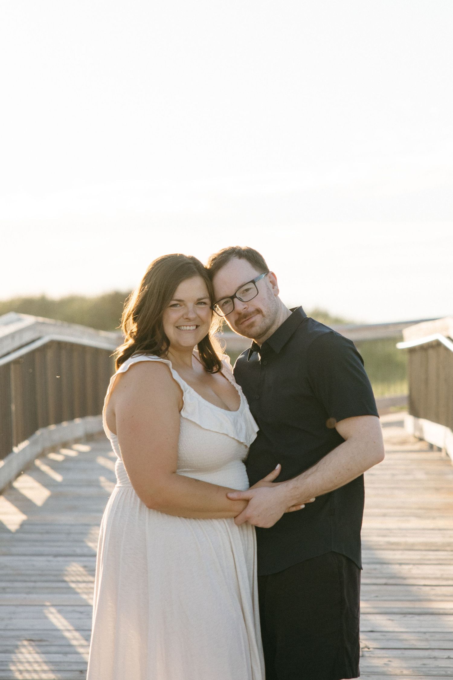 Happy couple embracing on a wooden boardwalk at sunset during a beach engagement session.