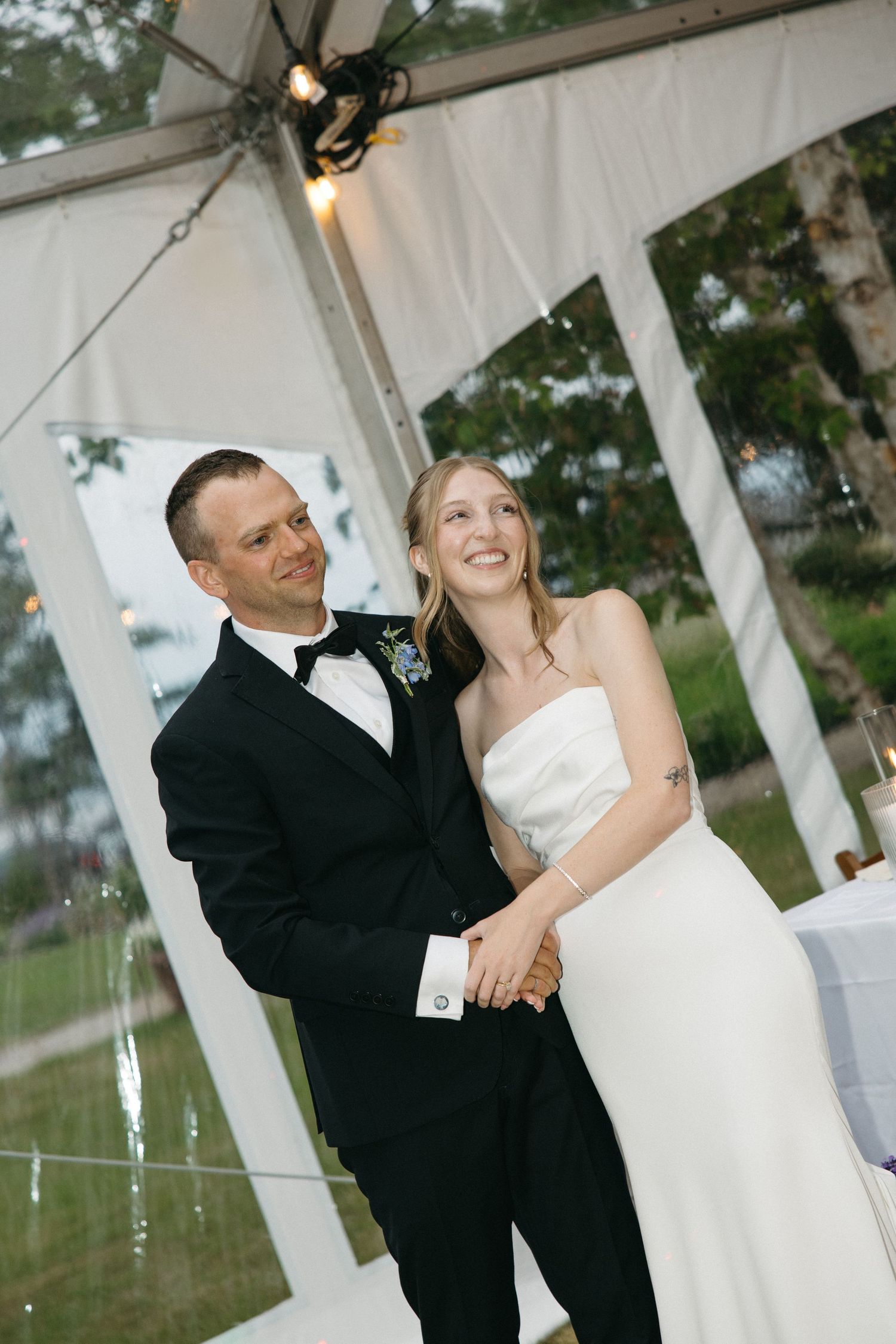 Bride and groom share a tender first dance moment under a clear tent with string lights at reception.
