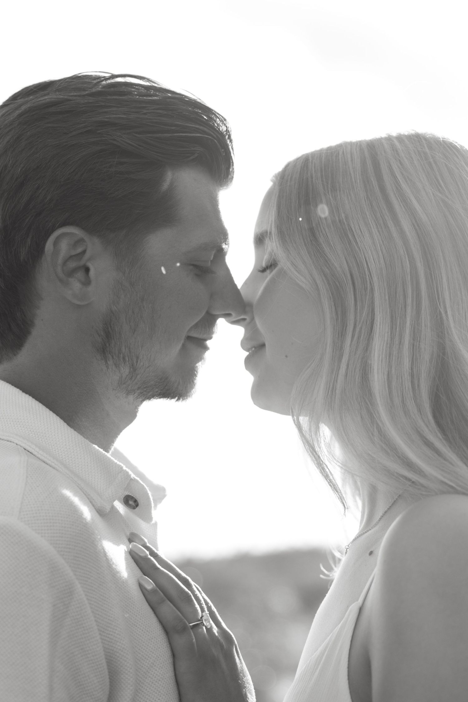 Black and white photo of a romantic couple about to kiss, faces close together in soft backlit lighting.
