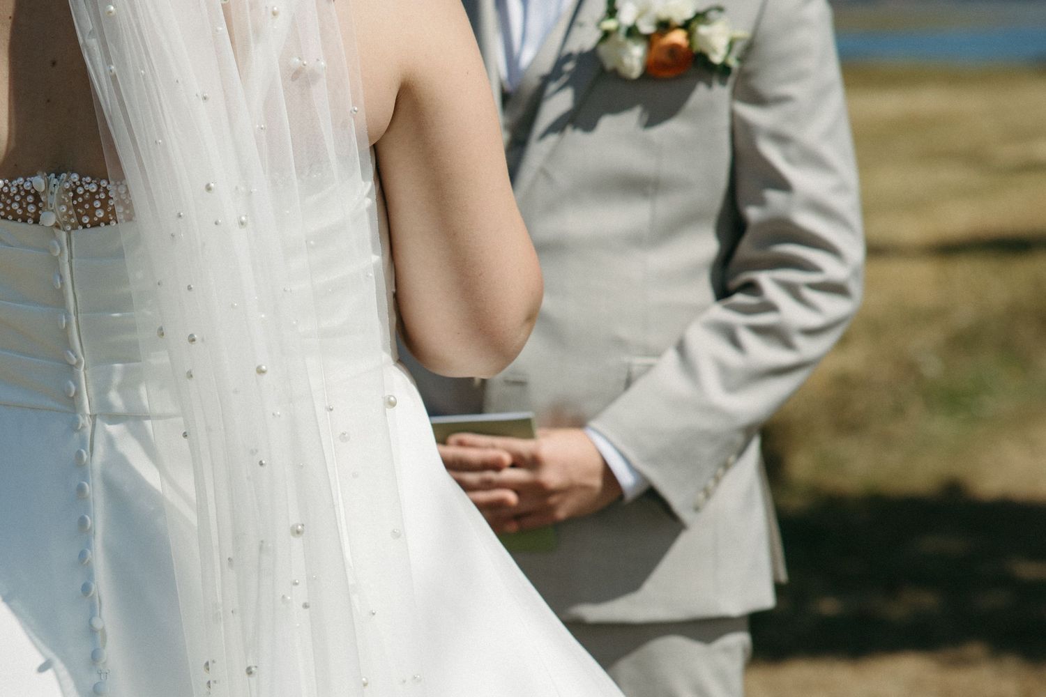 Close-up of bride and groom holding hands during outdoor wedding ceremony.