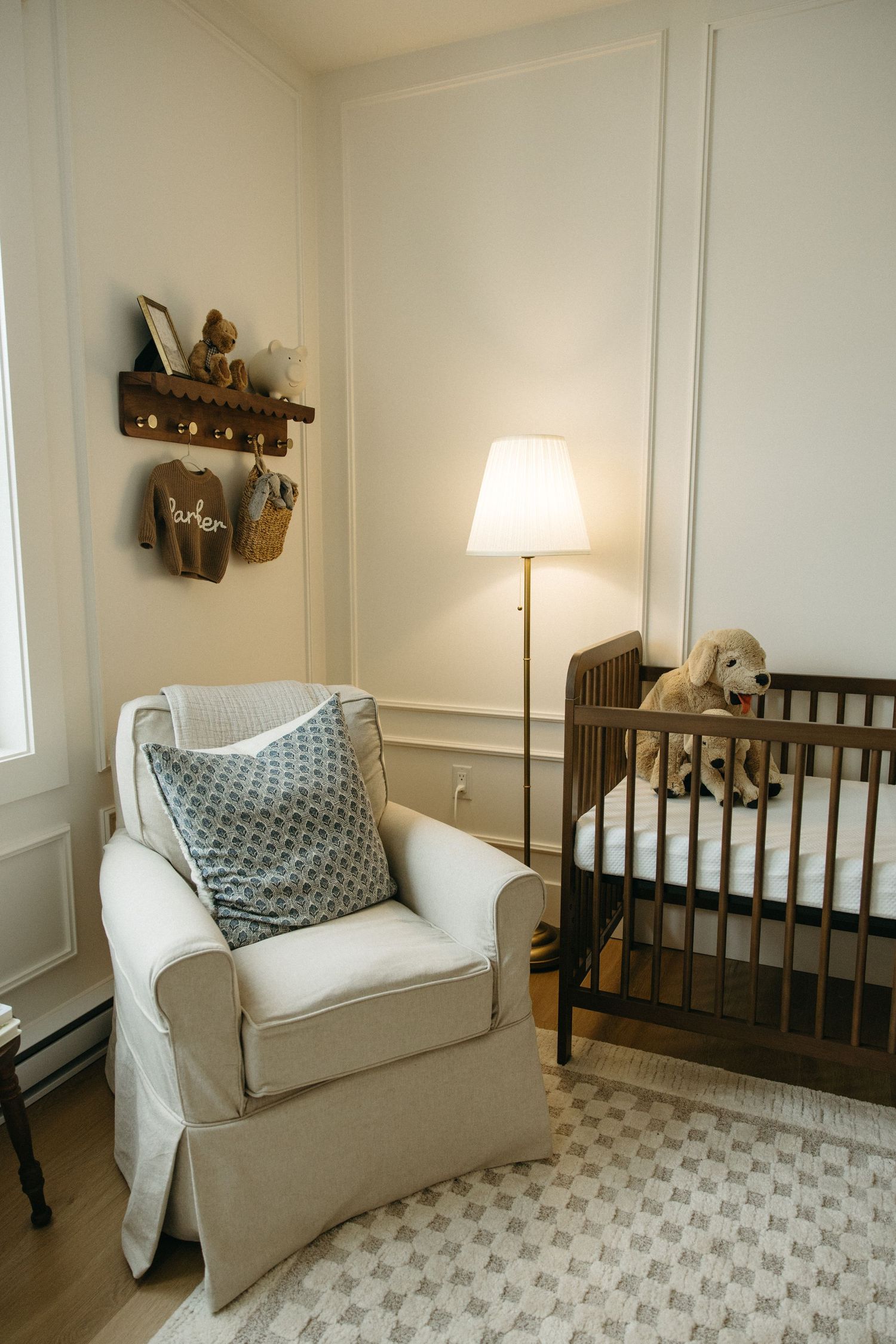 Neutral nursery room with white armchair, wooden crib, and soft gray accents.