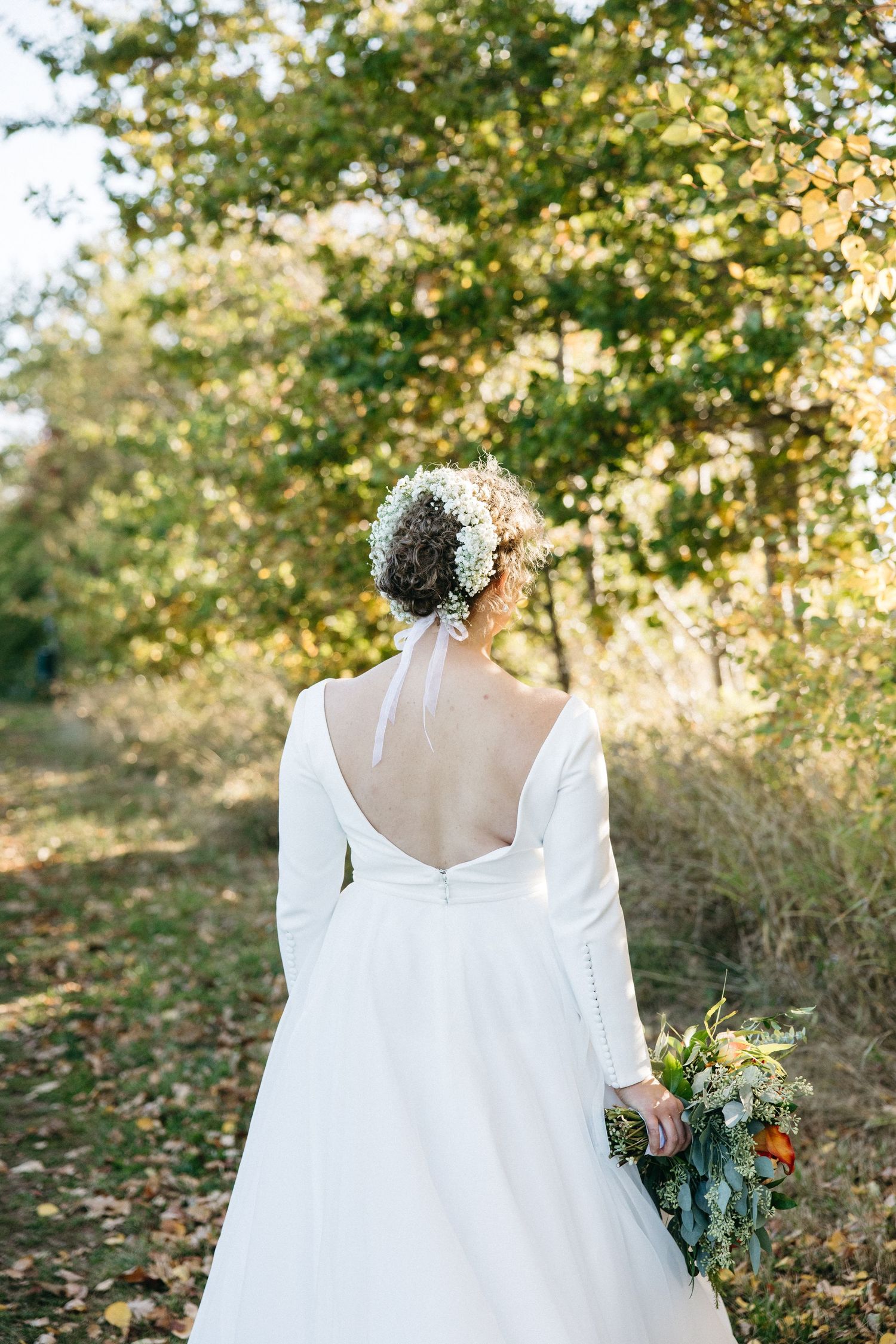 A white wedding dress photographed from behind in a sunlit autumn garden setting.