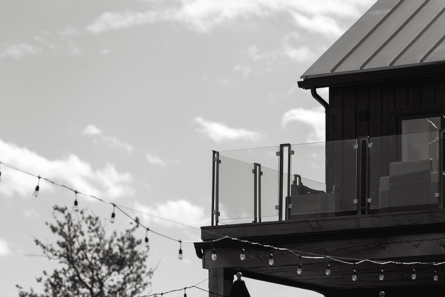 Modern barn-style building with string lights and metal roof against cloudy sky.