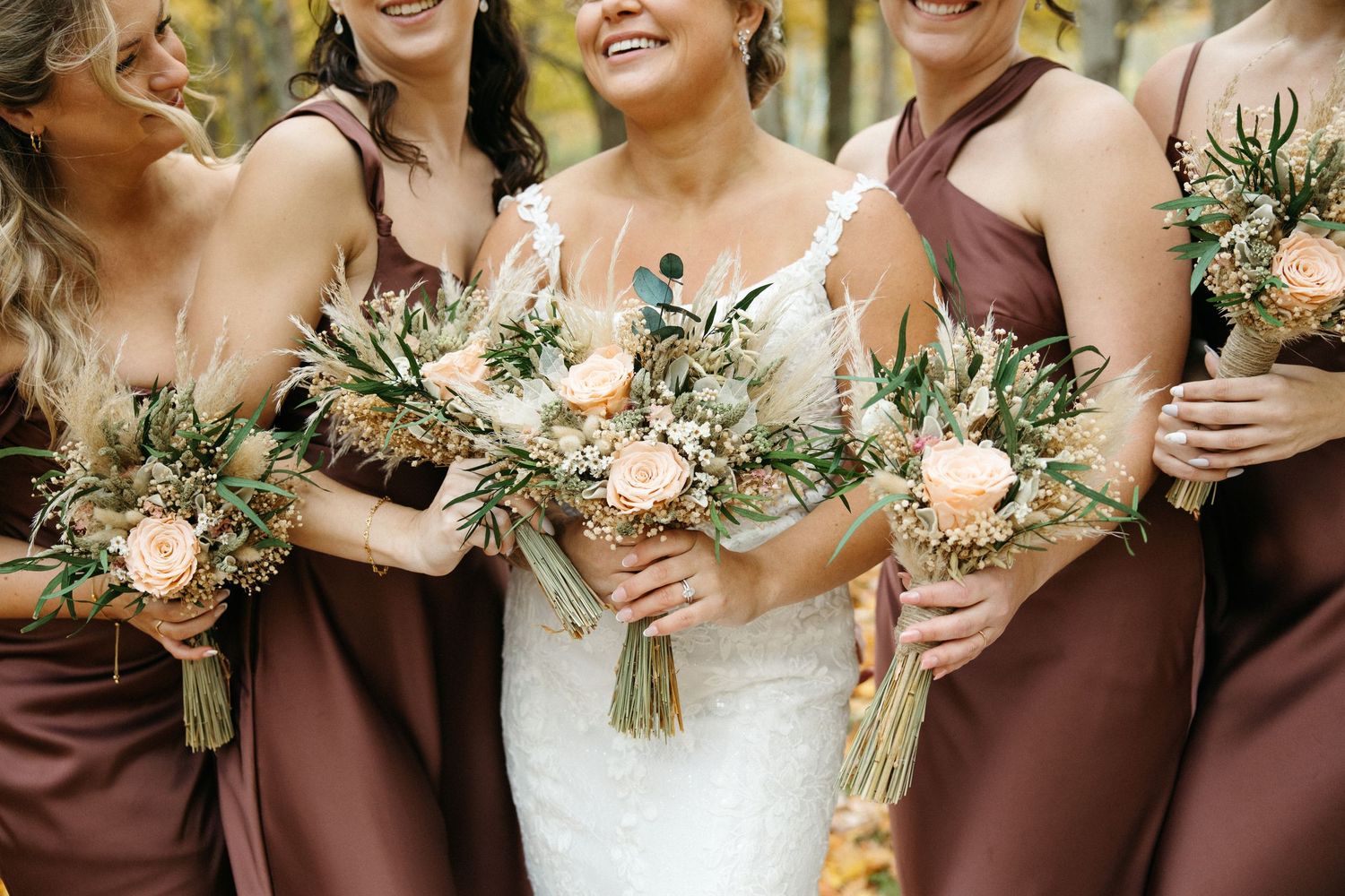 Bridesmaids in burgundy dresses holding floral bouquets at outdoor wedding.