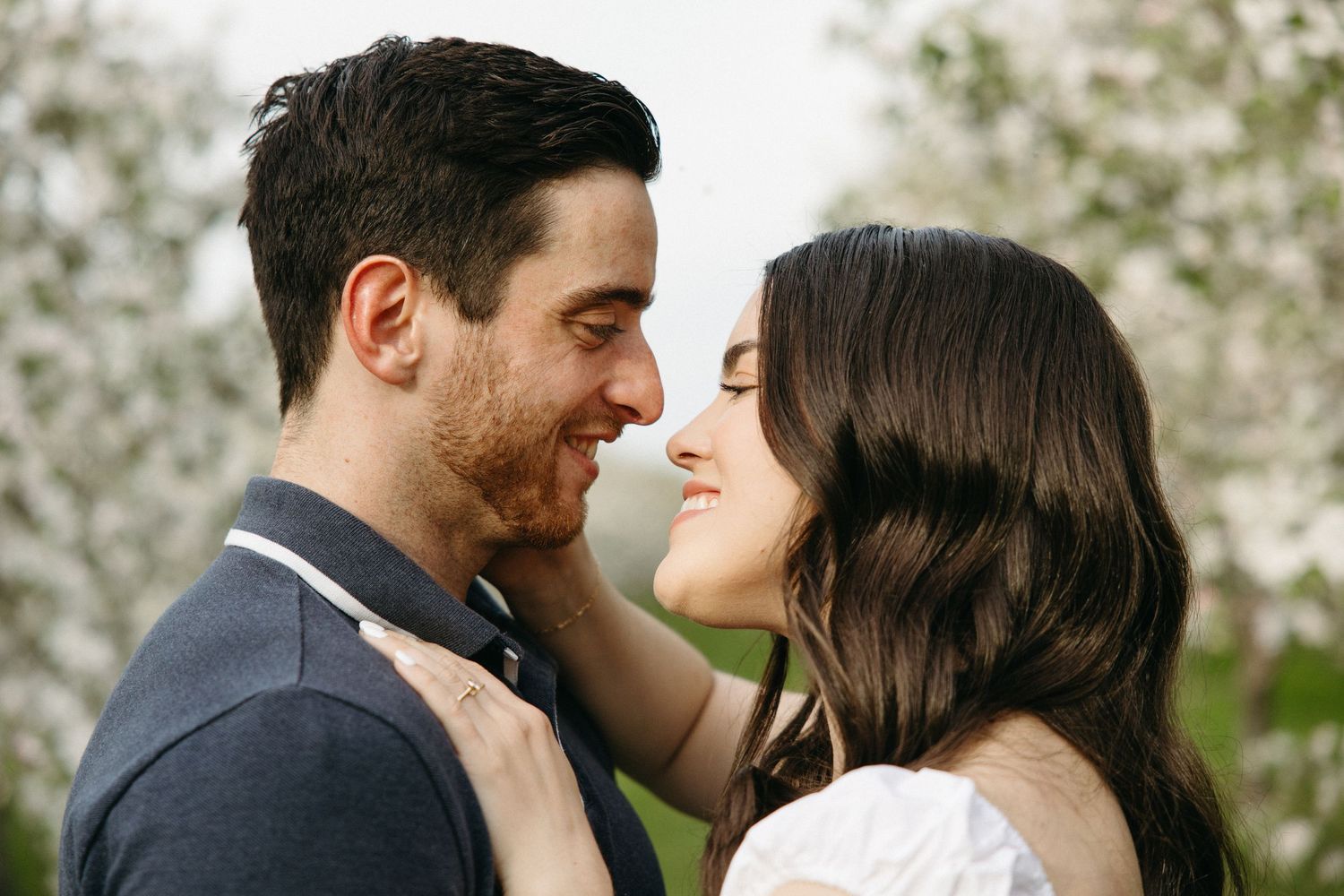 Happy couple sharing a close romantic moment, smiling at each other outdoors near white blooms.