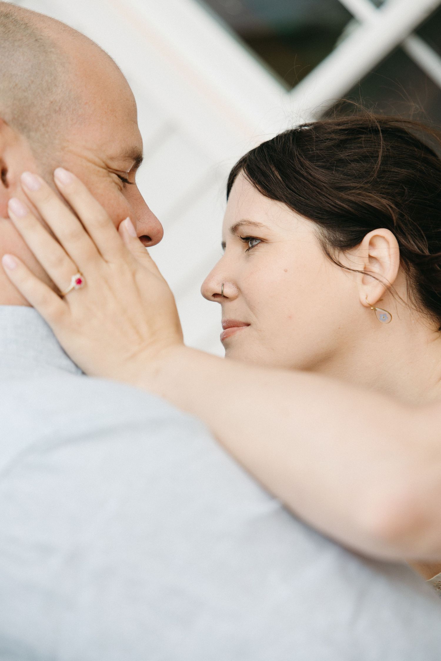 A woman gently touches a mans face as they gaze into each others eyes up close.