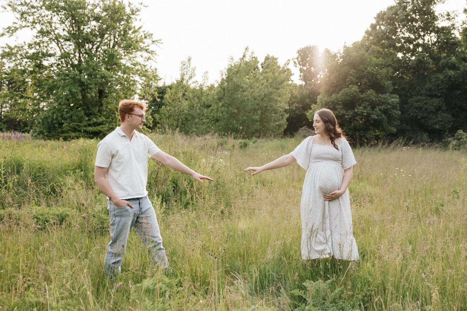 Couple enjoying a romantic moment together in a sunlit meadow with tall grass and trees in the background.