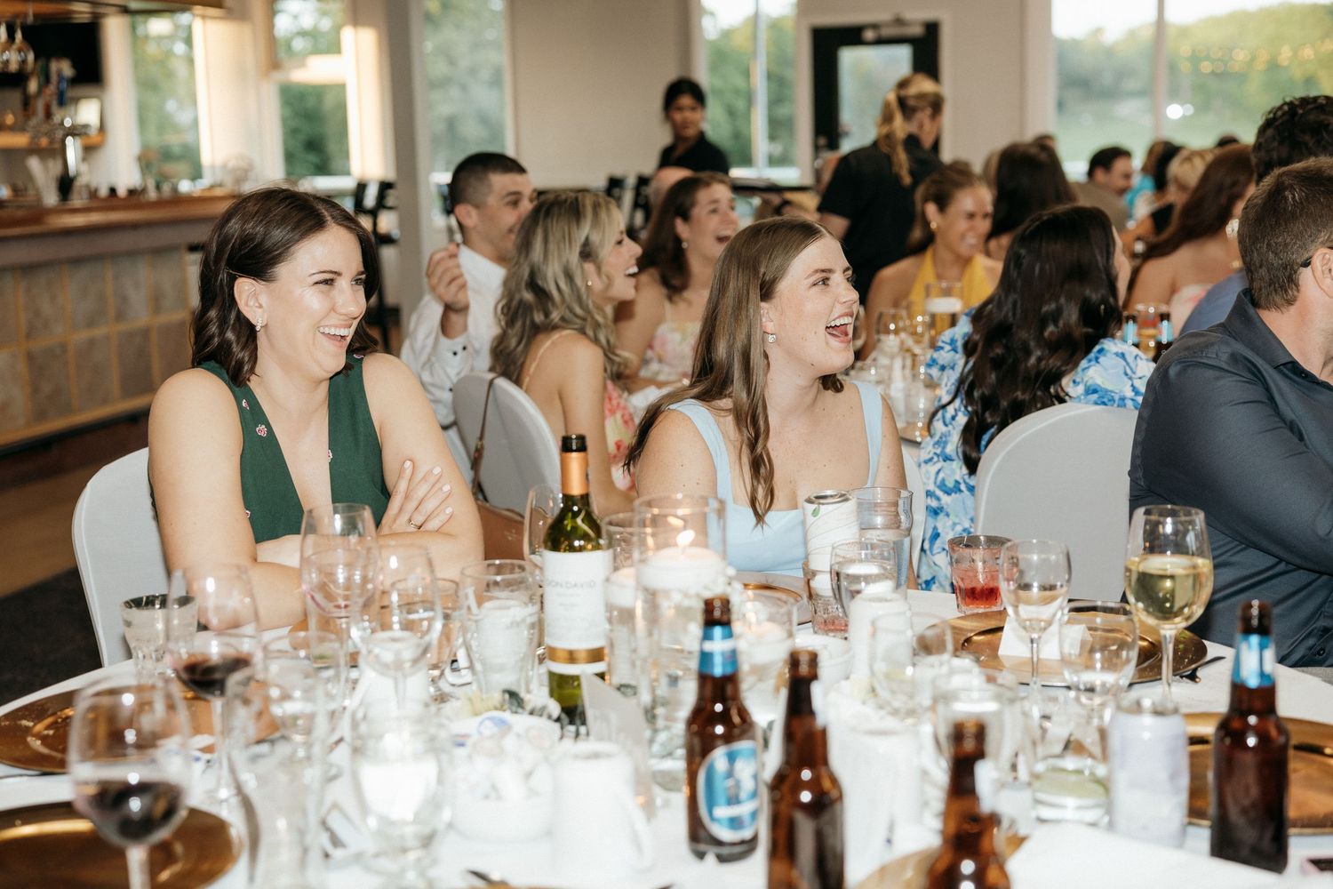 Wedding guests seated at tables with wine glasses and drinks during reception dinner.
