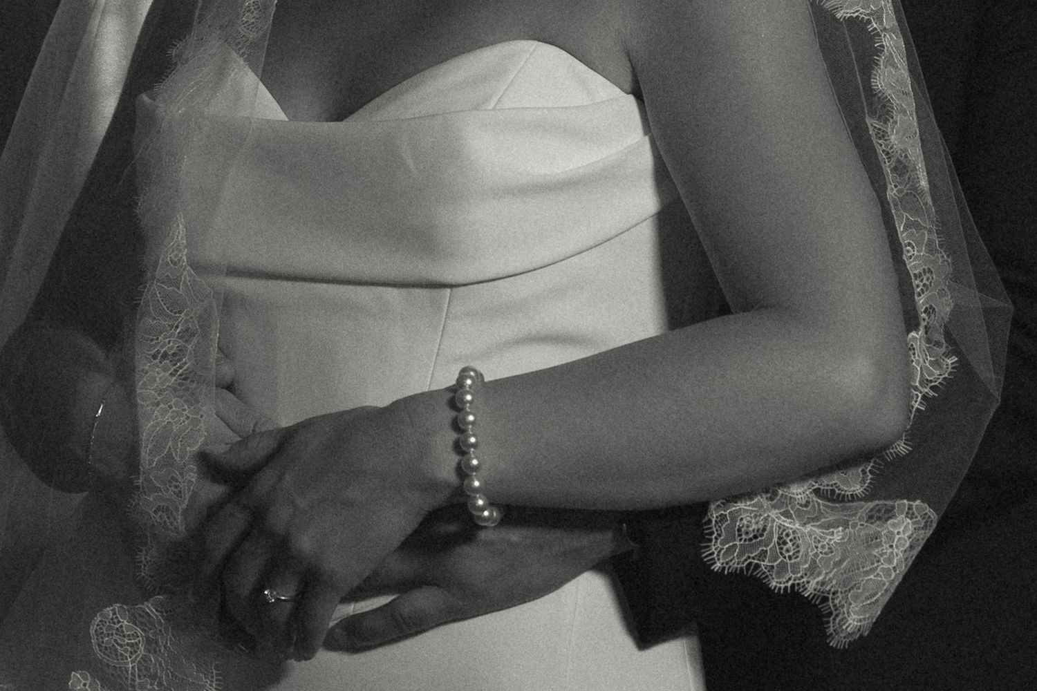 Black and white detail shot of bride's bracelet and lace sleeve against white wedding dress.