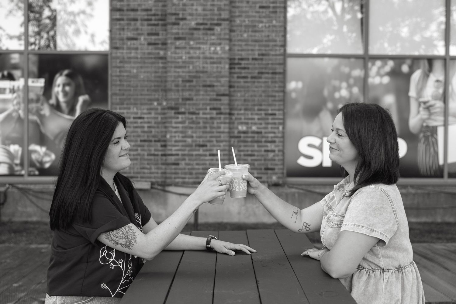 People enjoying beverages together at a black outdoor table against a brick building backdrop.