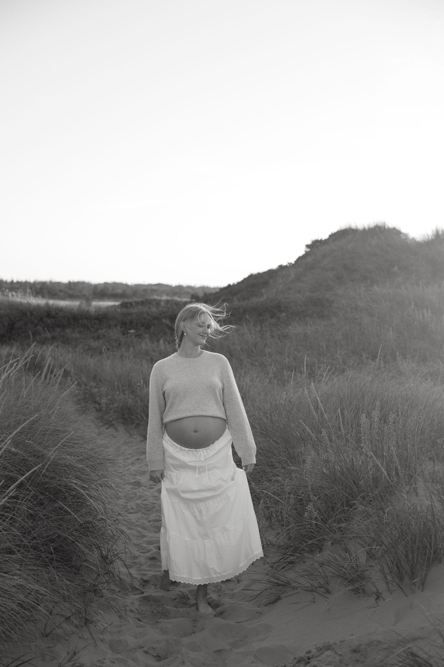 Dramatic black and white maternity silhouettes photographed in natural dune landscape.