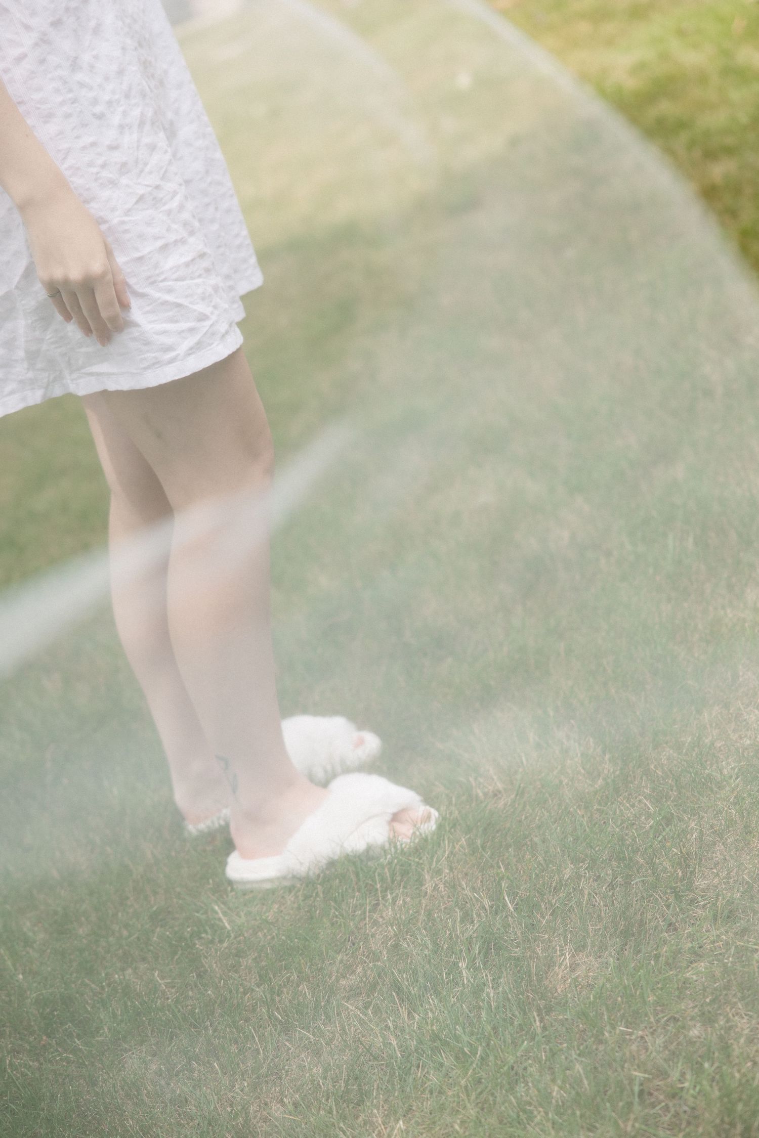 A woman in a white lace dress and fluffy slippers stands on green grass, partially obscured by a transparent bubble.