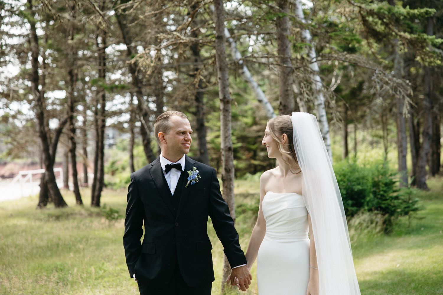 Bride and groom walk hand in hand through a lush forest setting on their wedding day.