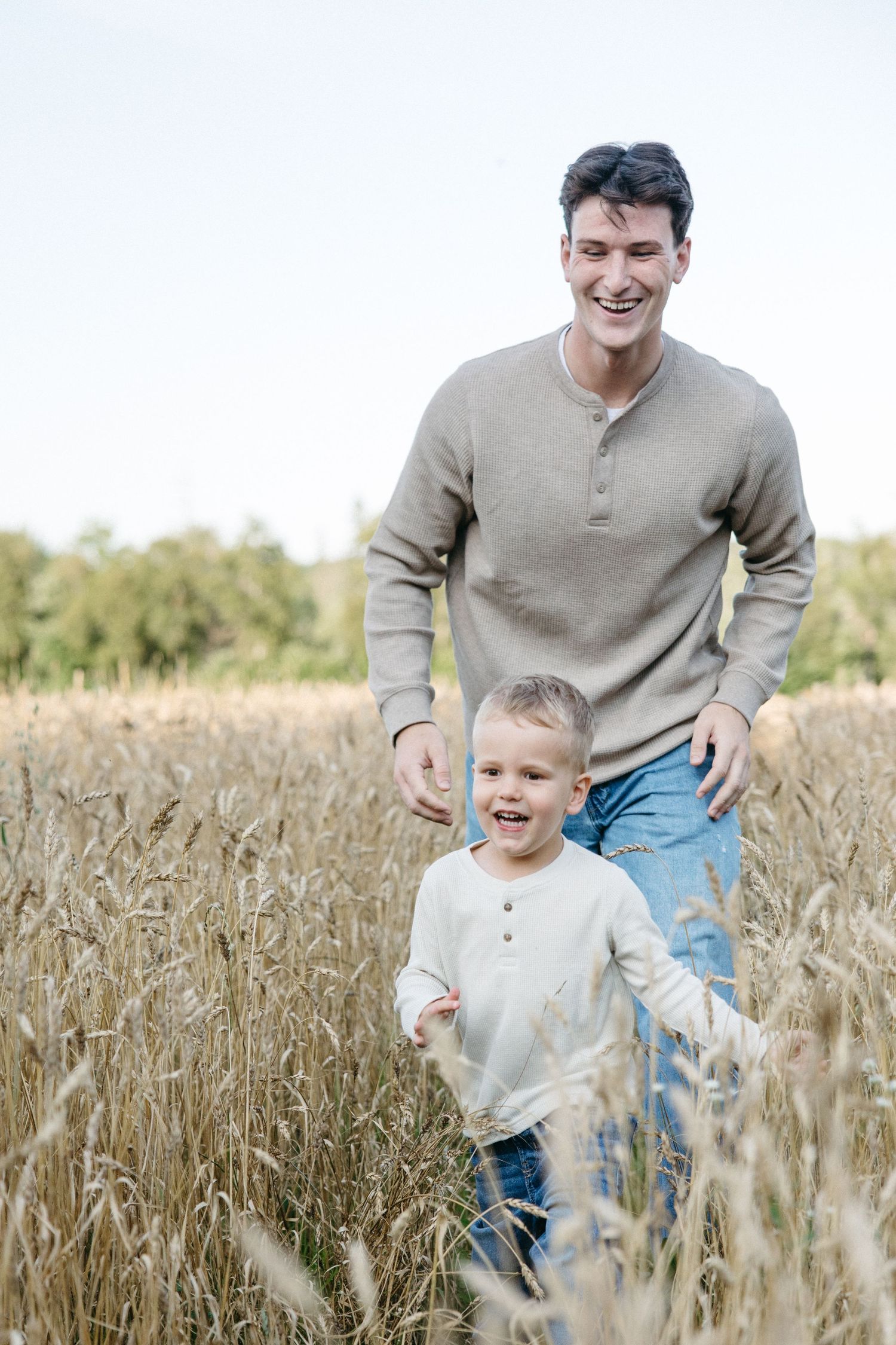A smiling father and young son walk together through a golden wheat field on a sunny day.