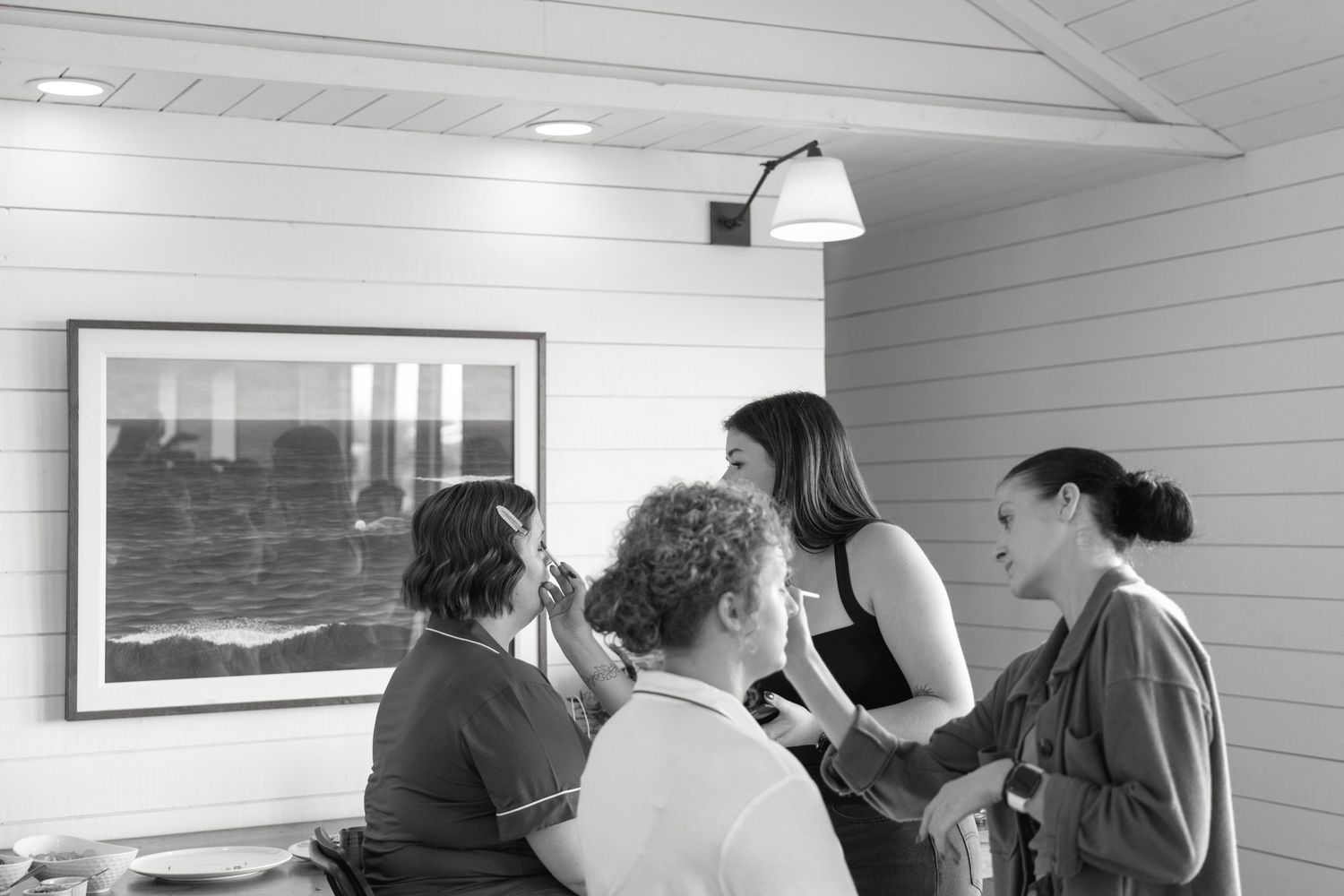 Group gathered in a coastal room looking at framed ocean artwork on white shiplap walls.