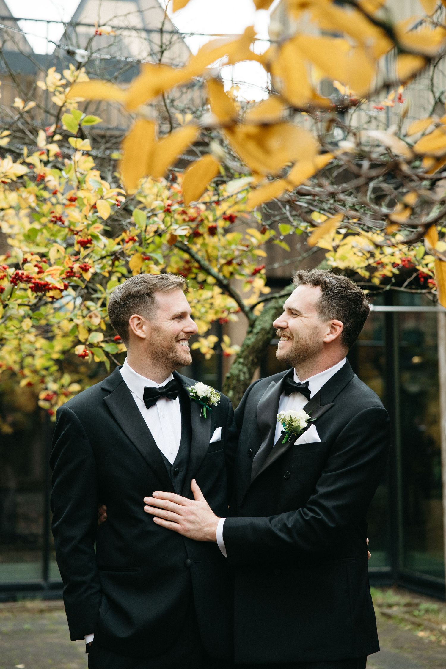 A joyful moment shared between two people in formal black tuxedos under fall leaves.