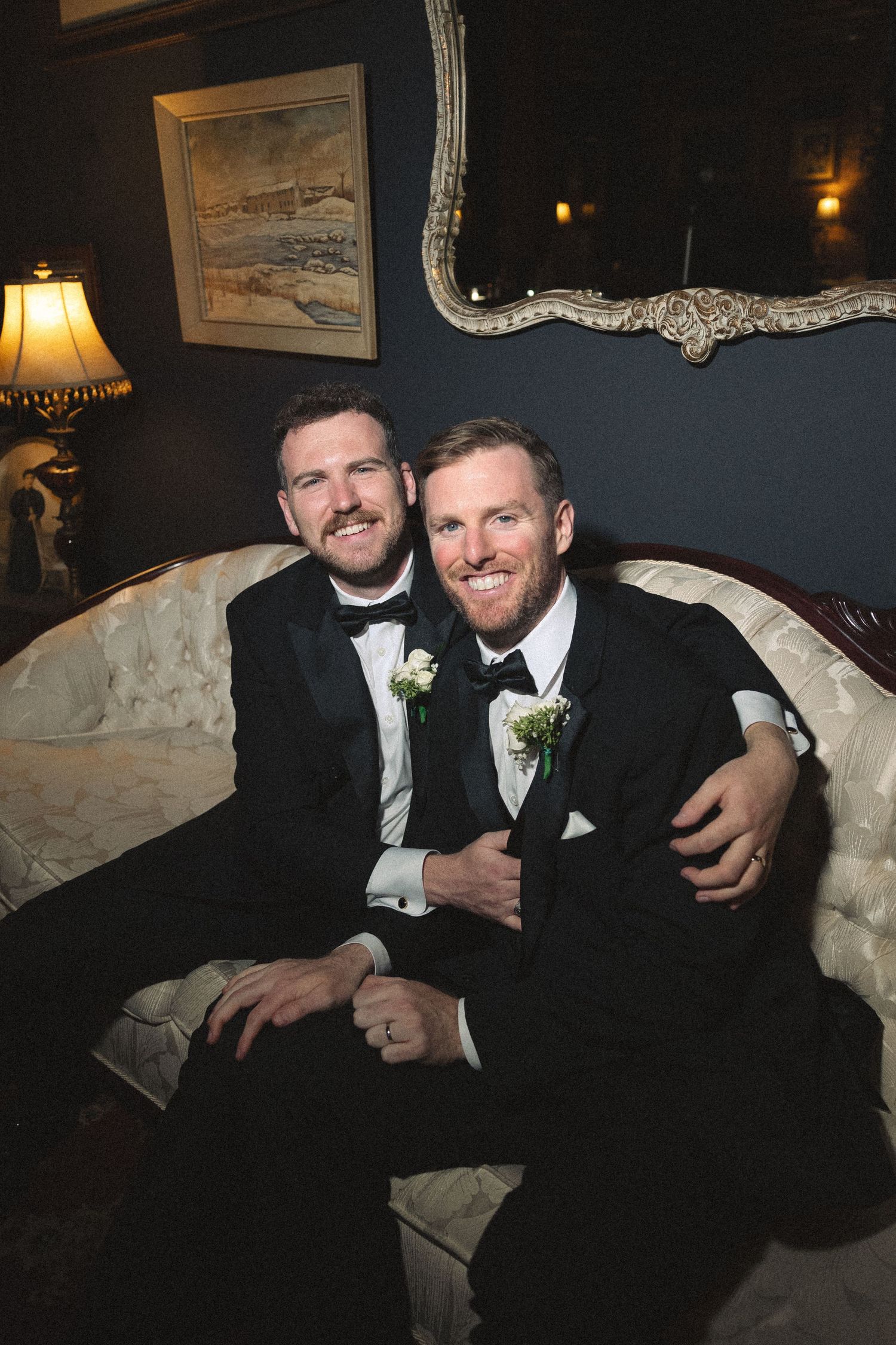 Two people in formal attire sharing drinks and conversation on an elegant white sofa.