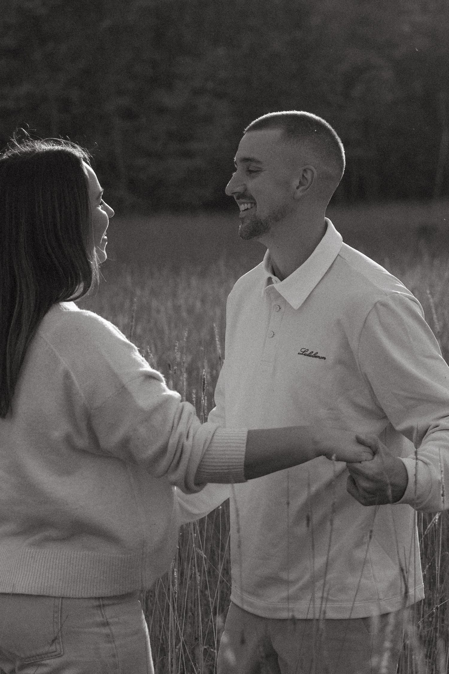 Black and white photo of two people dancing in a tall grass field.