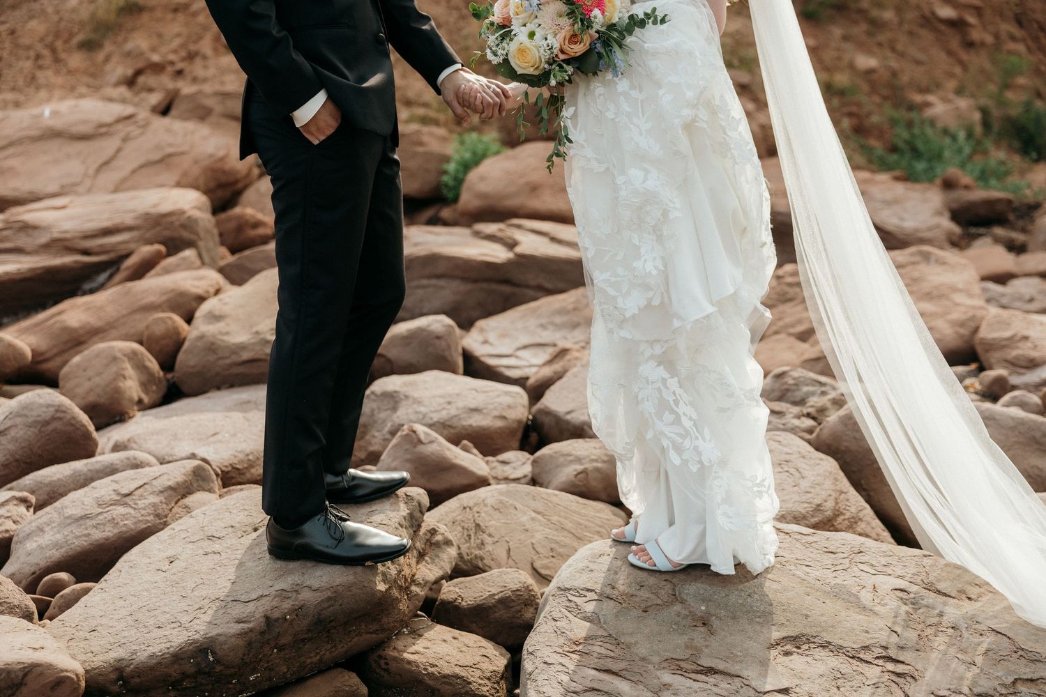 Close-up of bride and groom's formal attire while standing on rocky terrain.