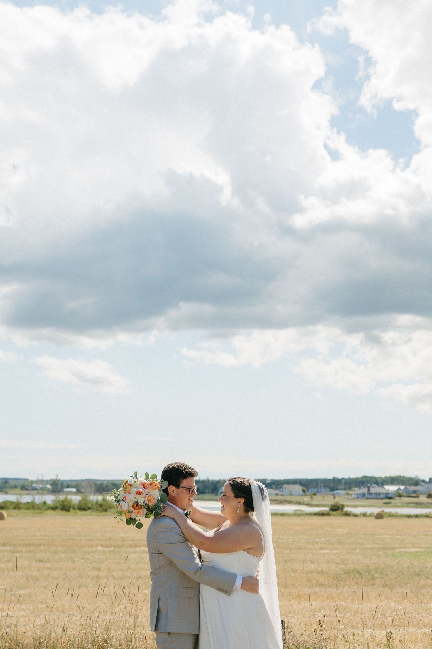 Bride and groom share a romantic moment in a golden field under dramatic clouds on their wedding day.