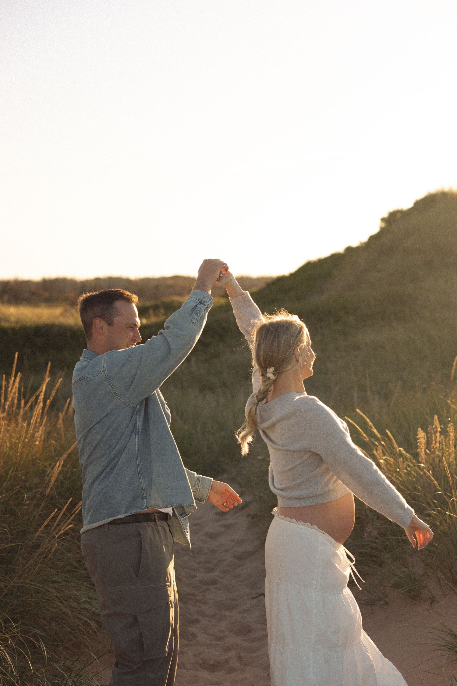 A couple dancing together in golden sunlight among sand dunes and tall grass.