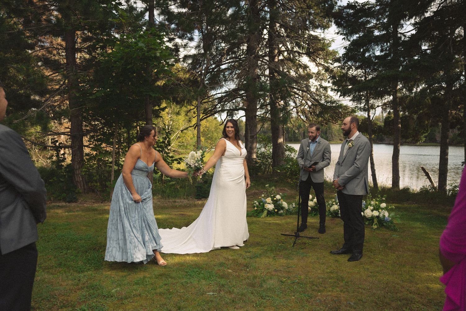 Scenic outdoor wedding ceremony setup with pine trees and water views in the background.