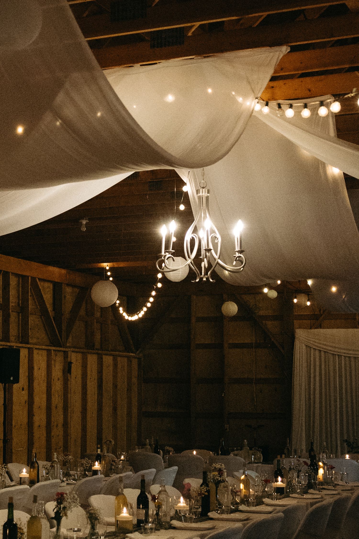 Rustic barn wedding venue decorated with white draping and romantic string lights overhead.
