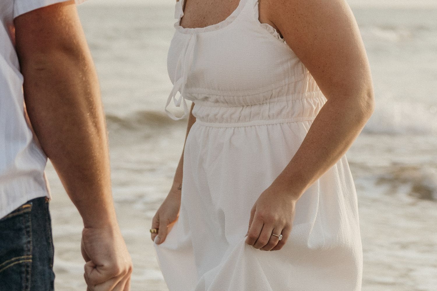 Two people's feet and legs walking in shallow ocean water at sunset.