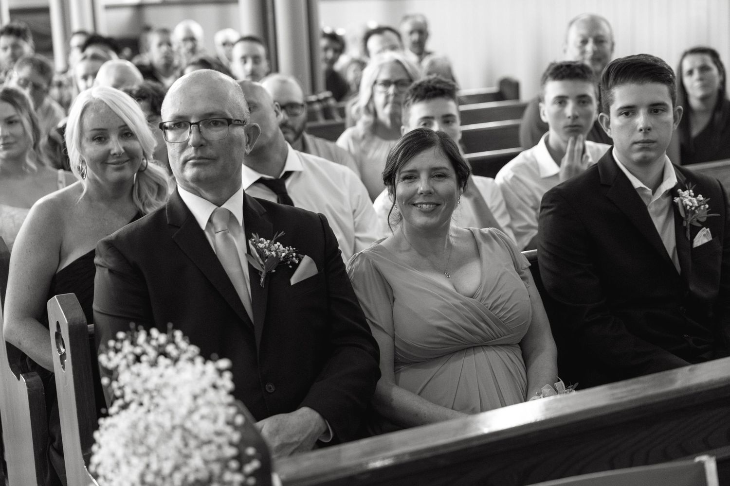 Black and white image of wedding guests reacting during ceremony in church pews.