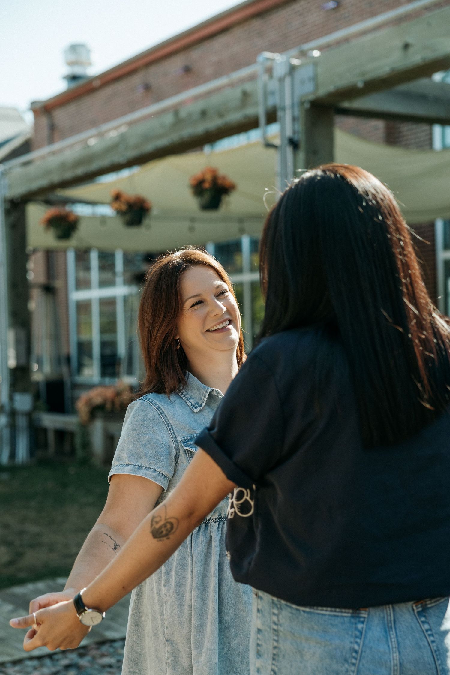 Two people laughing together on wooden steps outside a brick building.