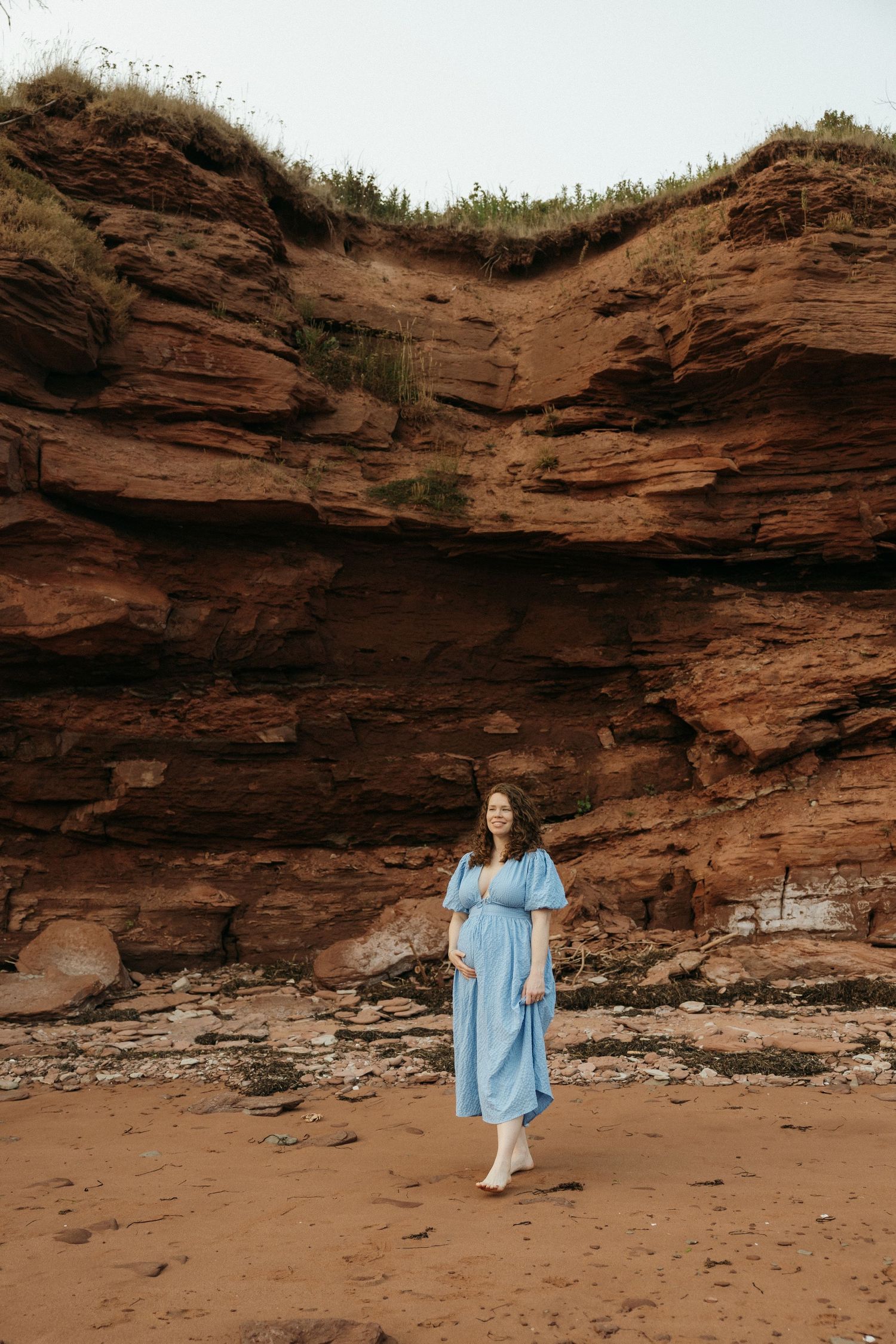 Someone in a flowing blue dress poses near dramatic red sandstone cliffs during a photo session.