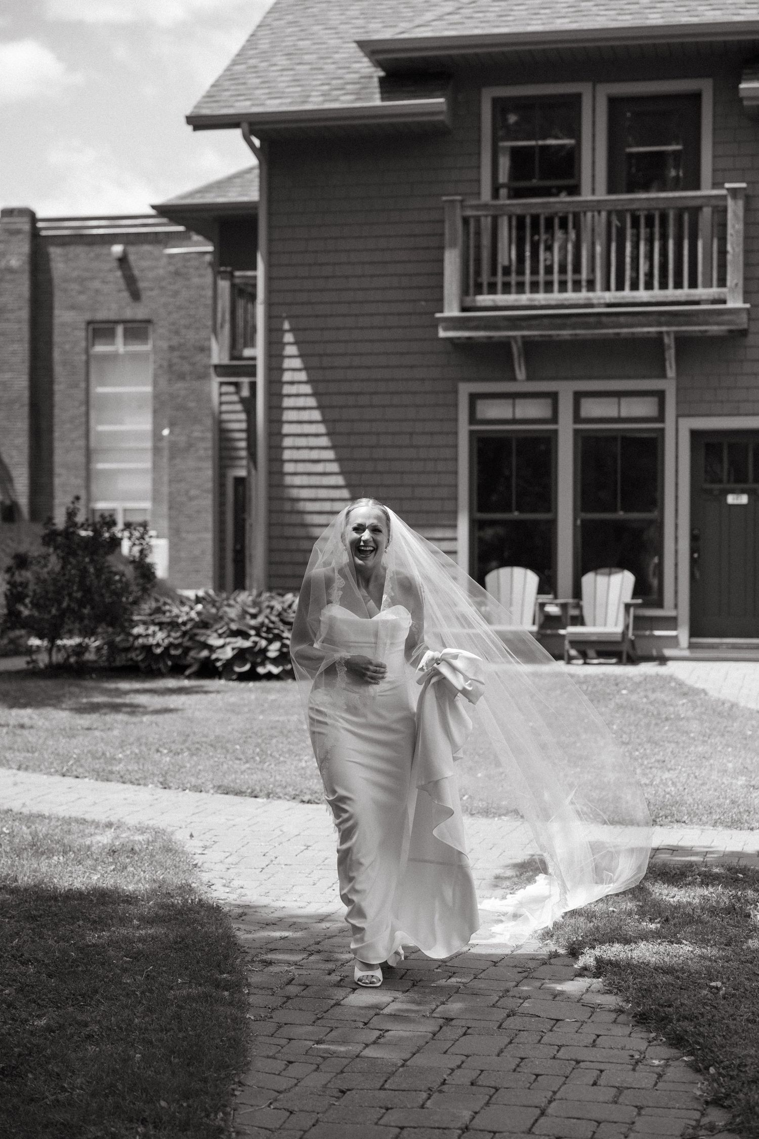 Flowing white wedding dress movement captured in black and white against house exterior.