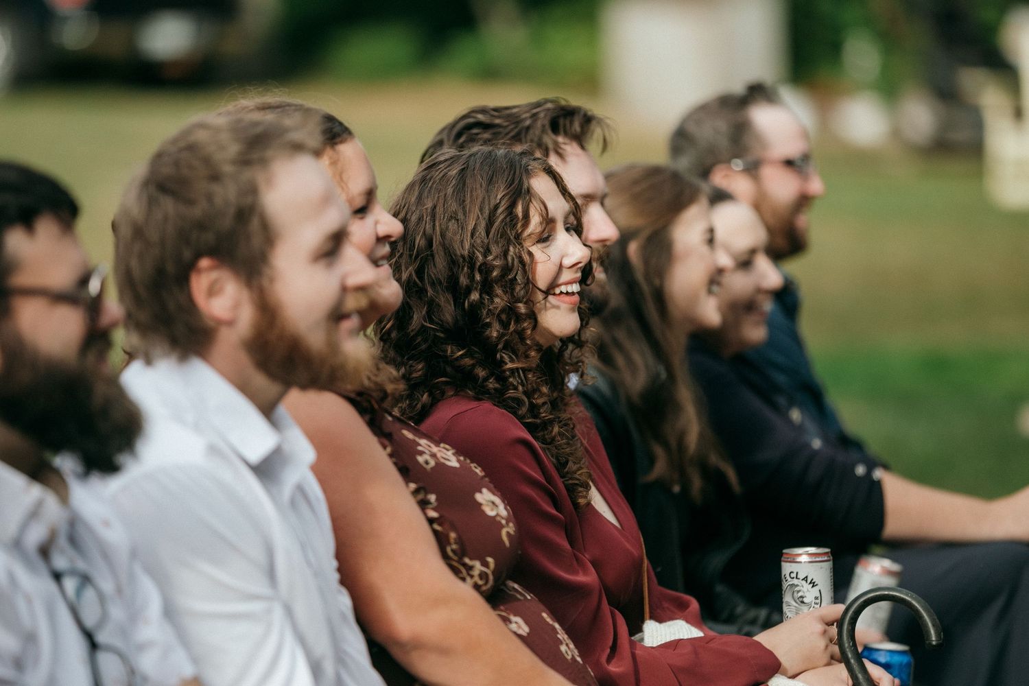 Wedding guests share joyful laughter while sitting outdoors on a sunny day.