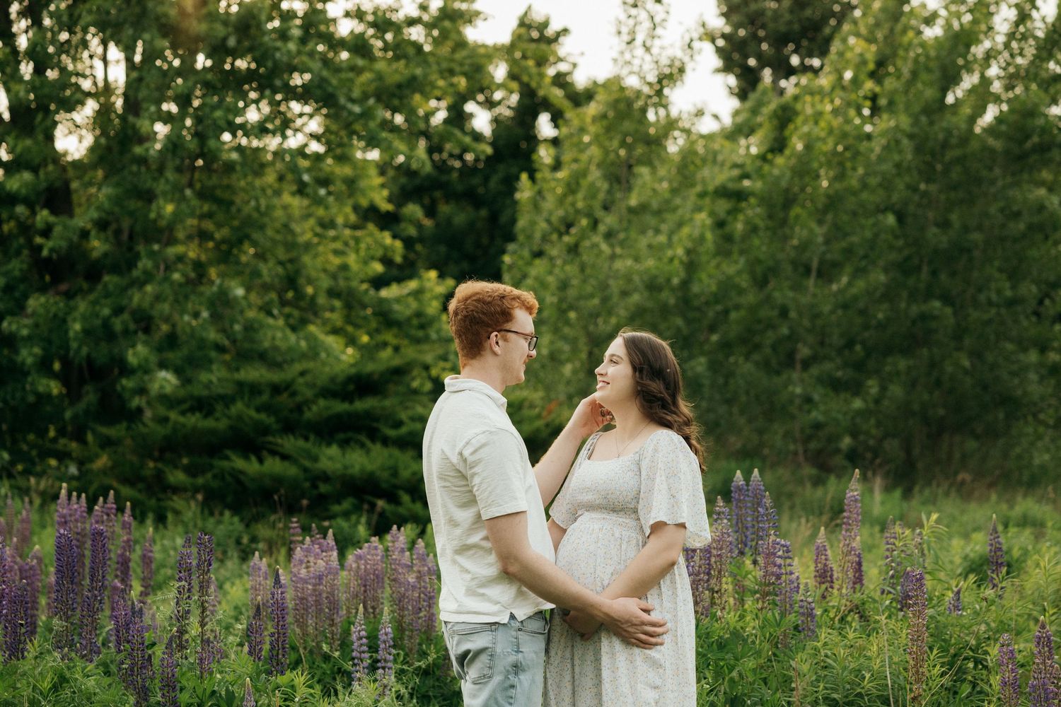 A couple shares a tender moment in a field of purple wildflowers during golden hour.