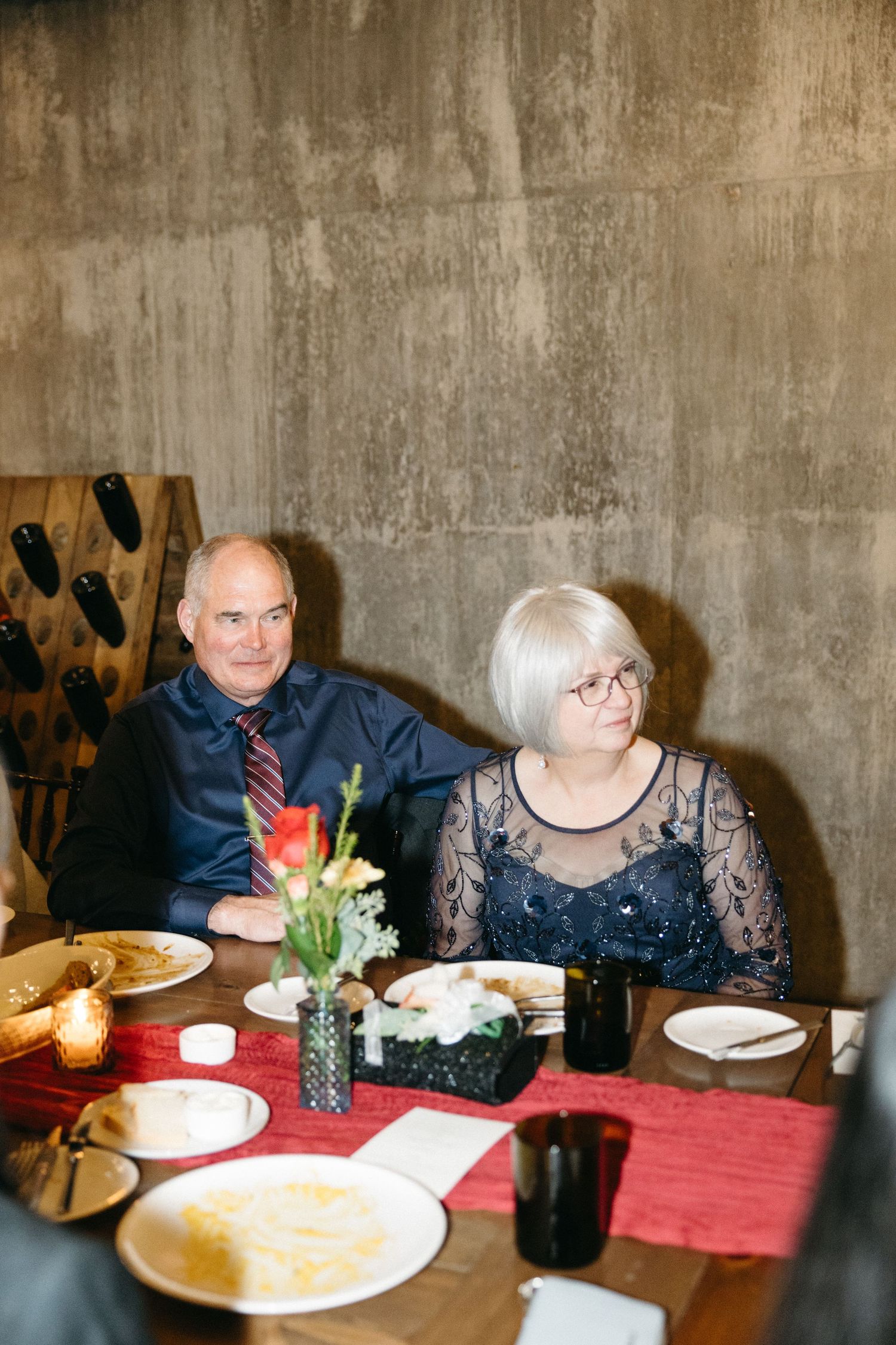 Dinner party guests seated at a table with red tablecloth and candlelight in a wine cellar setting.