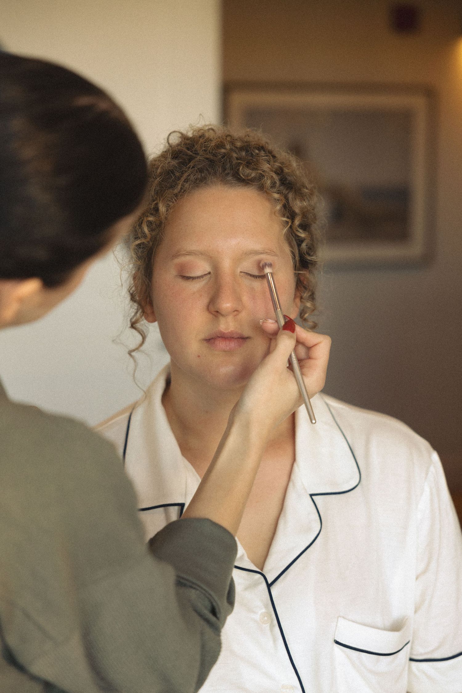Makeup artist applying eye makeup to client wearing white robe with black trim.