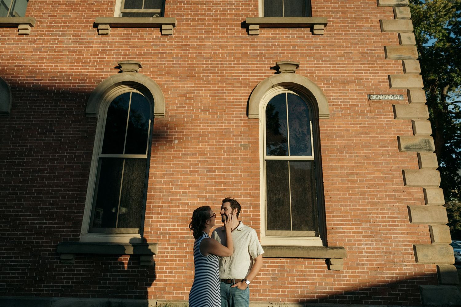 Intimate moments captured against the backdrop of a brick building with architectural details.