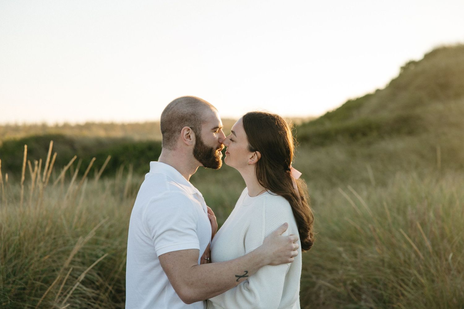 Romantic moment captured between couple in coastal dunes during sunset.